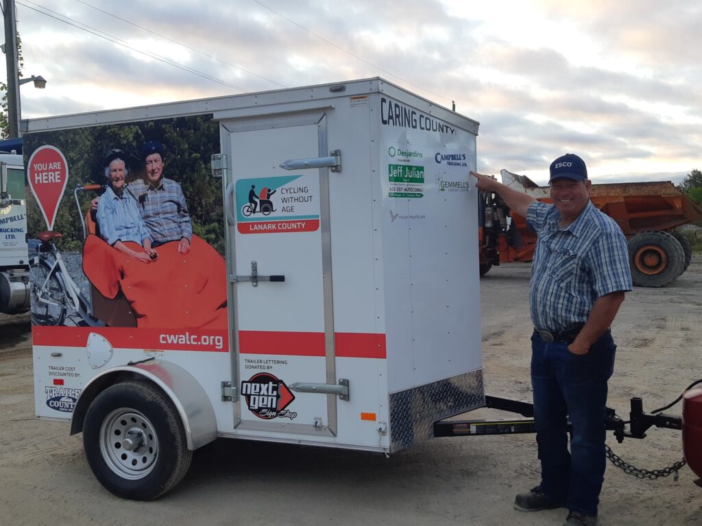 Bob Campbell of Campbell's Trucking pointing to his company's logo on the Trishaw trailer